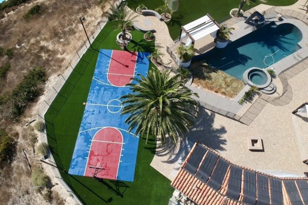 Aerial of San Diego estate property with pool, synthetic turf basketball court, and pavers
